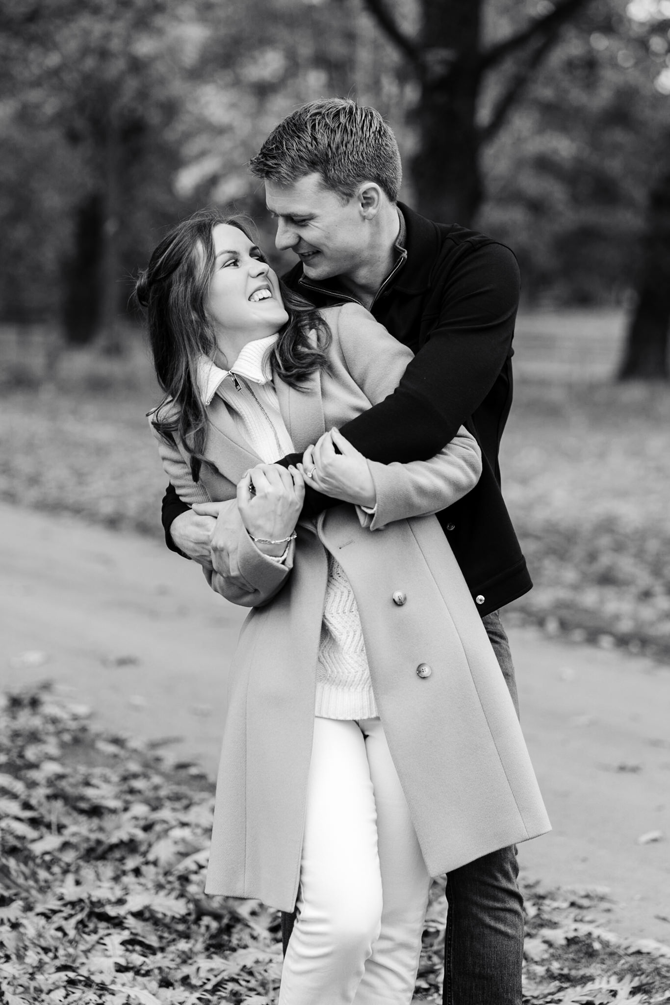 black and white portrait of a couple embracing with leaves on the floor in the background