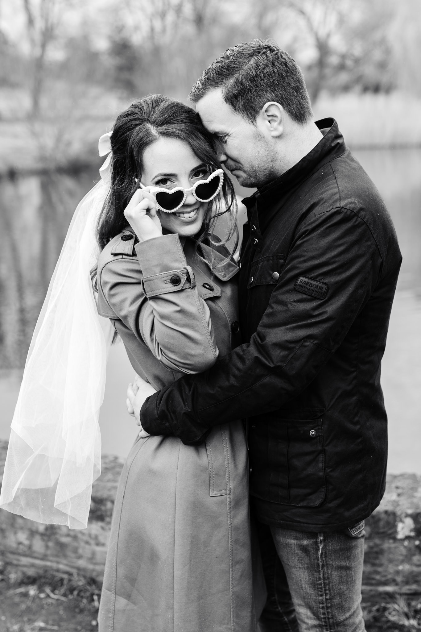 couple embracing and the bride to be peering over heart shaped glasses during their engagement session in hampshire