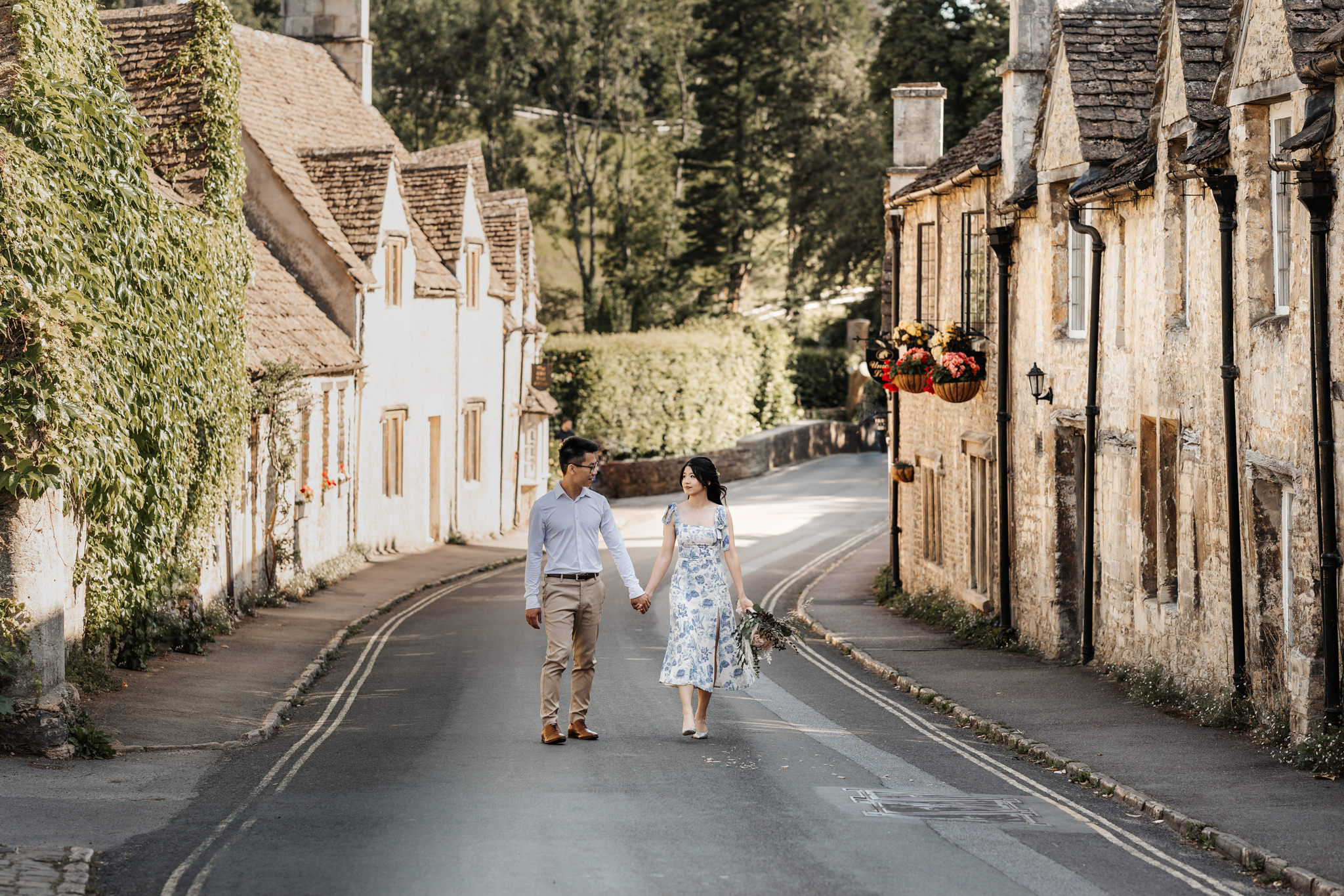 couple walking hand in hand through a small town in the cotswolds