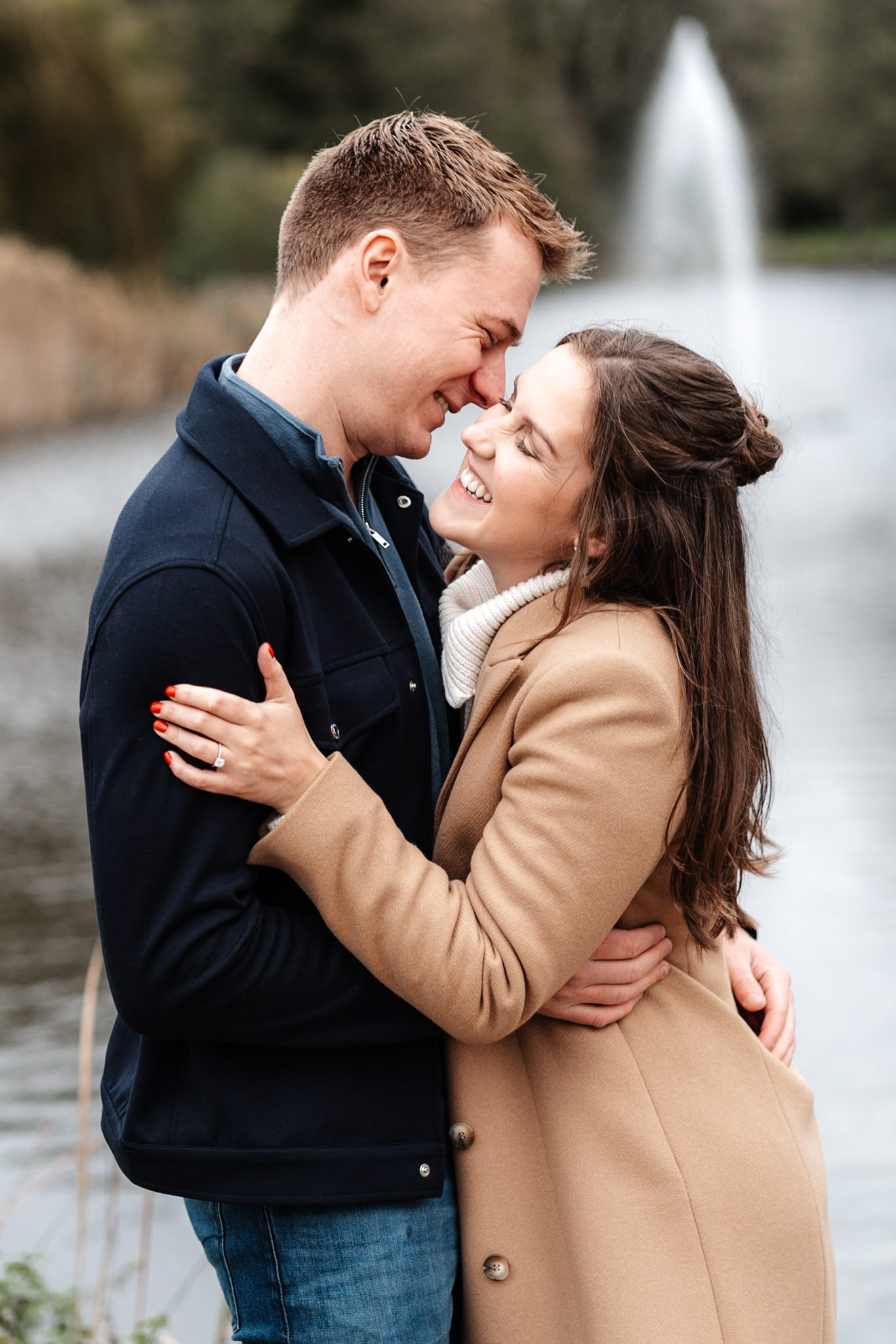 engaged couple laighing together with a beautiful lake and water fountain in the background