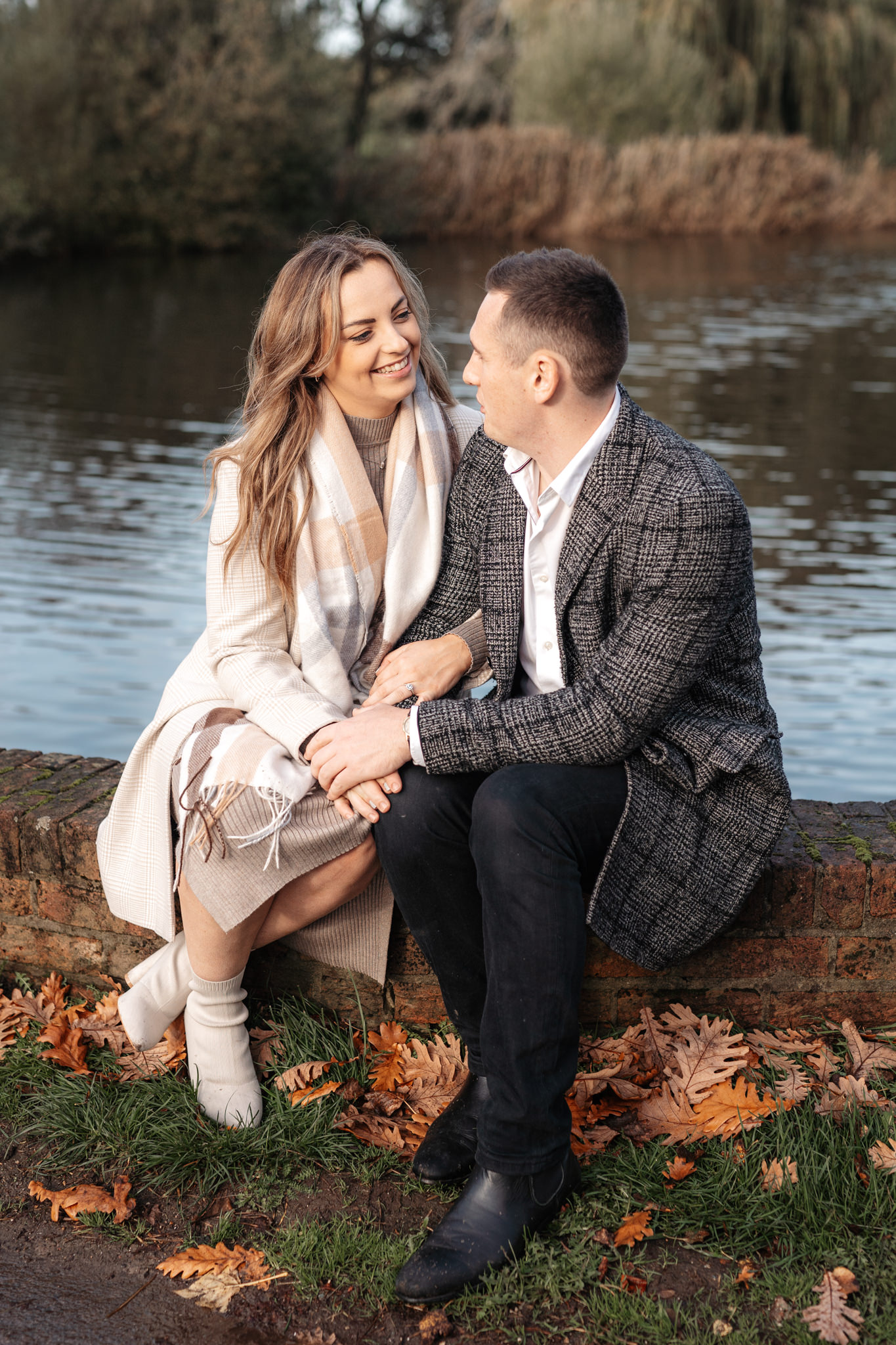 engaged couple sitting in front of a lake during their engagement photography session in basingstoke
