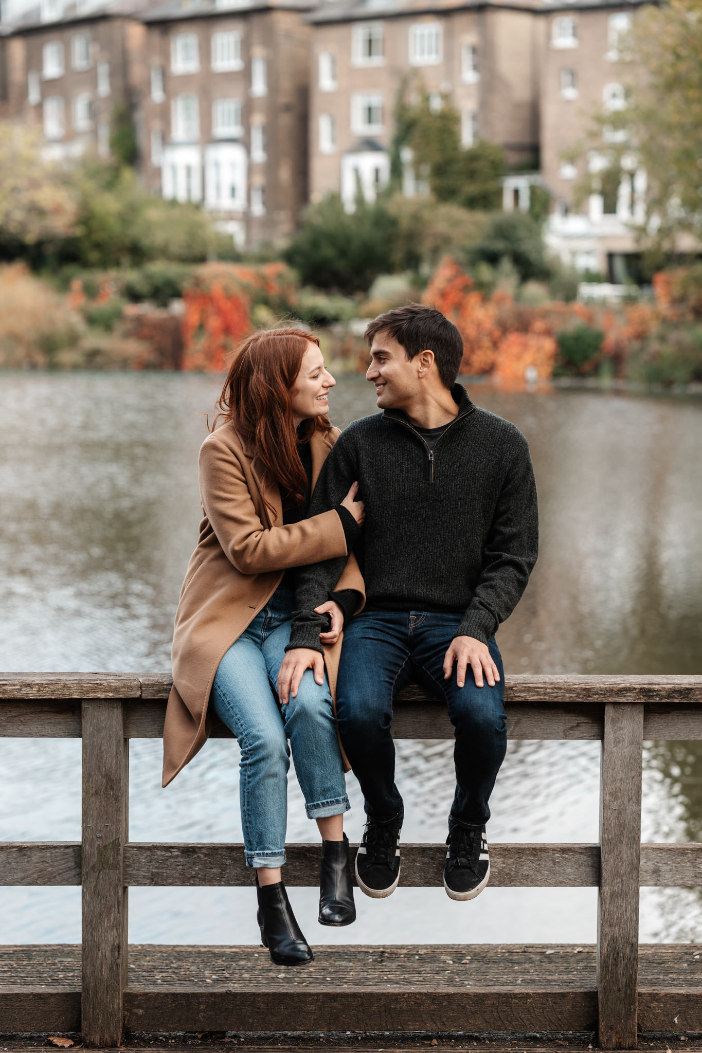 engaged couple sitting on a fence in front of a river during their london engagement photography session